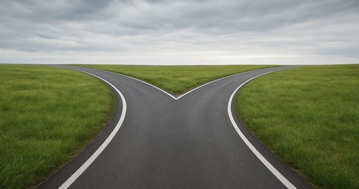 A two-lane road splitting into two directions surrounded by green fields under a cloudy sky.