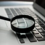 A magnifying glass resting on a laptop keyboard, emphasizing close examination